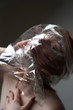Portrait of a young redhead girl on grey background with a plastic bag on her head. The concept of plastic pollution of nature. Excess plastic in a person's life