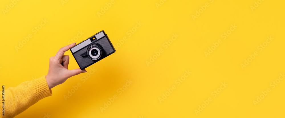 Woman's hand holds an old film camera on a yellow background, panoramic mock-up with space for text - obrazy, fototapety, plakaty 