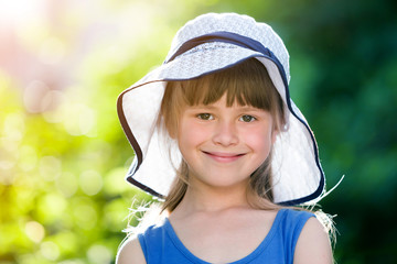 Wall Mural - Close-up portrait of happy smiling little girl in a big hat. Child having fun time outdoors in summer.