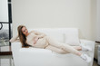 © Andrii - A pregnant girl is lying on the sofa in the living room and swinging her belly. Pregnancy and taking care of the child's future