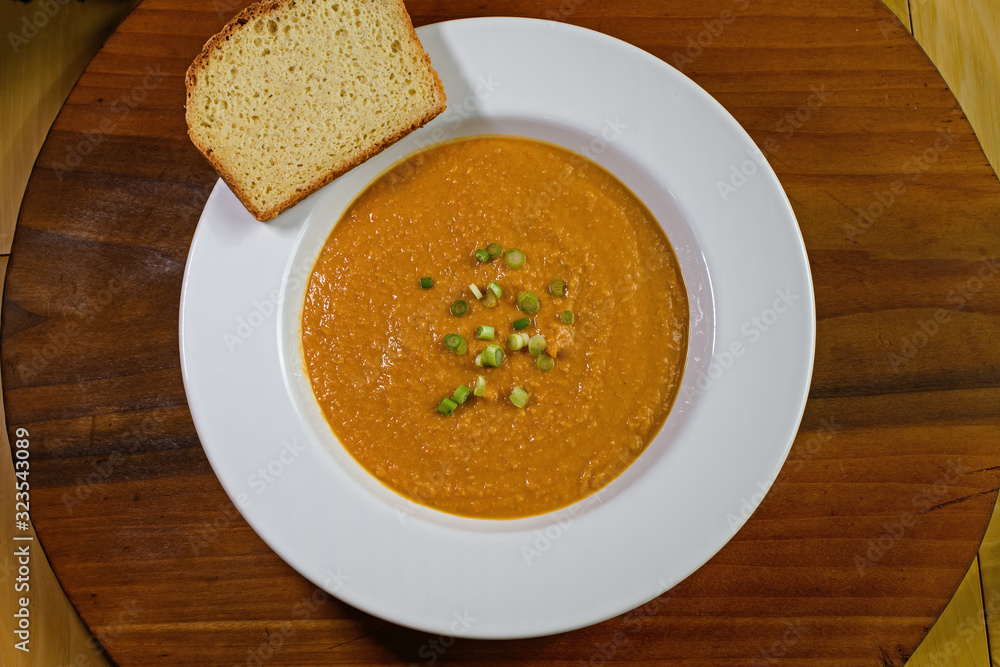 Vegetarian, gluten free peanut soup or groundnut soup in bowl with slice of gluten free bread. It is made from peanuts, carrots, sweet potatoes and scallions. It is a staple of African cuisine.