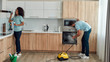 © Svitlana - Keeping your house clean. Two young professional cleaners in uniform working together in the kitchen. Young caucasian man using steam cleaner, happy afro american woman cleaning kitchen range hood.