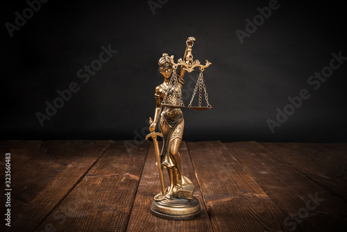 Themis symbol of justice, courts on wooden countertop and dark background. The concept of justice and dealing with court cases. Problems of citizens in courts, honesty and winning cases with judges.