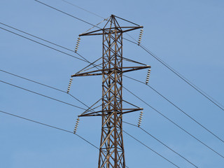 a high voltage electric power distribution tower against a light blue sky