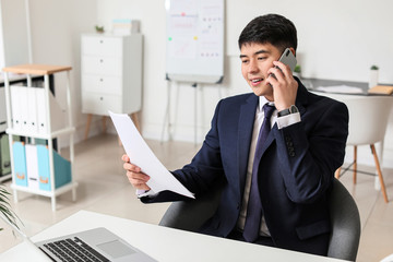 Poster - Young Asian businessman talking by phone in office