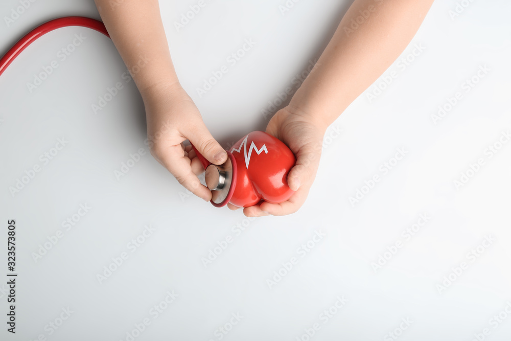 Child's hands with red heart and stethoscope on white background. Cardiology concept