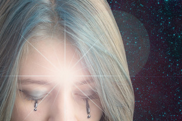 A young girl with a burning star on her forehead and downcast eyes against the starry sky. The concept of clairvoyance, mysticism, divination, divination. Elements of this image are provided by NASA.