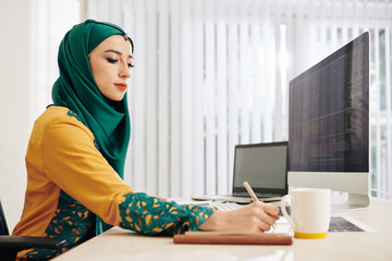 Wall Mural - muslim young woman taking notes in planner when working on programming code for new project