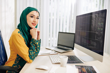 Wall Mural - beautiful young muslim woman in hijab sitting at office table in front on computer with programming 