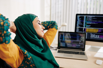 Wall Mural - young muslim woman stretching in her chair after working on programming code