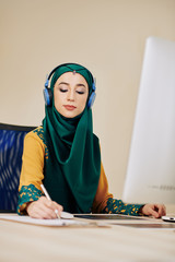 Wall Mural - female entrepreneur in hijab listening to music in headphones when working on project