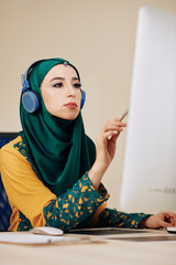 Wall Mural - serious female software developer in hedphones searching for mistakes in programming code on compute