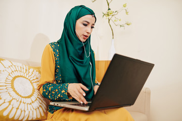 Wall Mural - muslim female entrepreneur wearing earbuds when making video call to business partner or client to d
