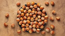 Hazelnuts In Shells Are Falling Onto A Black Ceramic Plate And Textured Bark Paper Background, Stop Motion Animation