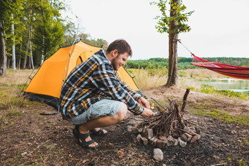 Wall Mural - young strong man light a fire at camping site yellow tent on background