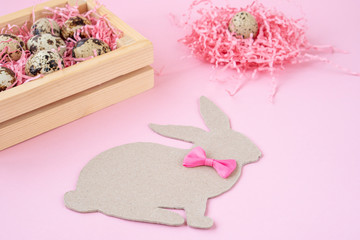 Easter eggs in a wooden box and nests. Easter Bunny with a pink bow. Easter gift with pink ribbon. Empty for a greeting card. pink background is creative.