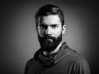 Wall Mural - Portrait of handsome man with beard and mustache. Close-up image of serious brutal bearded man on dark background. Black and white photography