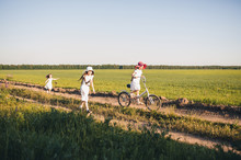 Children Joyfully Run After A Bicycle On A Field With Flowers