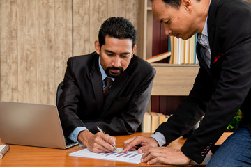 Young executive business man discussing to partner or colleague point investment strategy presentation on technology laptop, Asian mature beard man suit solve problem with employee in workplace