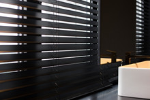 Wood Blinds Coulisse Black Color Closeup On The Window. Wooden Plate 50mm Wide. Venetian Blinds In The Bathroom. Black Tap, Mirror Near The Washbasin.