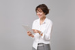 Cheerful young business woman in white shirt posing isolated on grey wall background studio portrait. Achievement career wealth business concept. Mock up copy space. Holding, using tablet pc computer.