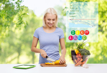 healthy eating, diet and people concept - happy smiling young woman chopping vegetables with calories, vitamins and food nutritional value over green natural background