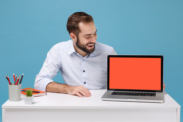 Cheerful young man in shirt sit at desk isolated on pastel blue background. Achievement business career concept. Mock up copy space. Work on project with laptop pc computer with blank empty screen.