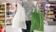 © Syda Productions - consumerism and eco friendly concept - woman holding reusable canvas tote for food shopping and plastic bag over supermarket on background