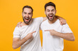 © ViDi Studio - Cheerful young men guys friends in white blank empty t-shirts posing isolated on yellow orange background in studio. People lifestyle concept. Mock up copy space. Pointing index fingers at each other.