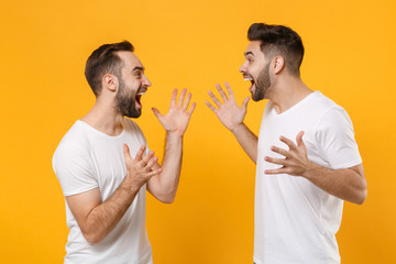 Canvas Print - Excited young men guys friends in white blank empty t-shirts posing isolated on yellow orange background in studio. People lifestyle concept. Mock up copy space. Looking at each other spreading hands.