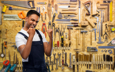 Poster - profession, construction and building concept- happy smiling indian worker or builder celebrating success over work tools on background