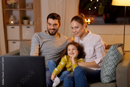 family, leisure and people concept - happy smiling father, mother and little daughter watching tv at home at night