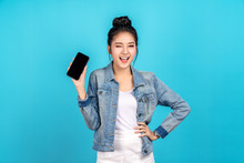 Happy Asian Woman Feeling Happiness, Blinks Eyes And Standing Hold Smartphone On Blue Background. Cute Asia Girl Smiling Wearing Casual Jeans Shirt And Connect Internet Shopping Online And Present