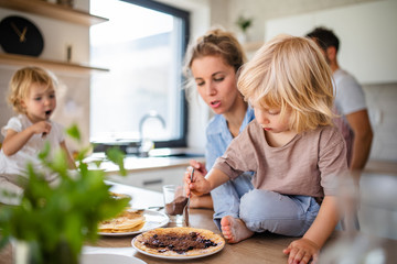 young family with two small children indoors in kitchen, eating pancakes.