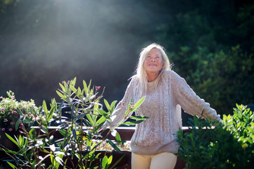 Senior woman standing outdoors on terrace, resting.