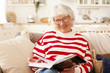 © shurkin_son - Leisure, self education, hobby and retirement concept. Picture of good looking mature senior female in striped sweater and stylish eyewear enjoying reading in living room, smiling joyfully