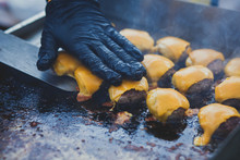 Process Of Cooking Different Multi Colored Burgers On Open-air Festival, View Of Chef Hands In Black Gloves With Variety Of Fillings And Ingredients On Wooden Desk And Stove
