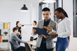 © anatoliycherkas - African businesswoman and Asian businessman using a tablet with interracial group of business men & women team