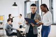 © anatoliycherkas - African businesswoman and Asian businessman using a tablet with interracial group of business men & women team