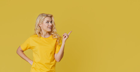 Wall Mural - Young happy woman shows hands up, spreads his hands to the sides. Above is an empty place for text and inscription on a yellow background.