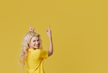 Wall Mural - Young happy woman shows hands up, spreads his hands to the sides. Above is an empty place for text and inscription on a yellow background.