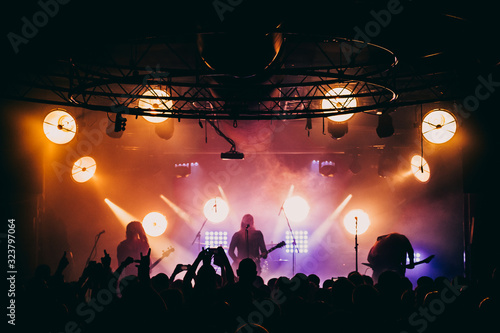 Metal band performing live on stage. Underground black metal gig. Stage lights shining behind musicians.