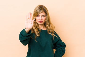 Young blonde caucasian woman standing with outstretched hand showing stop sign, preventing you.