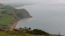 An Over-the-shoulder, Extreme-long Shot Of A Massive Body Of Water Meeting Grasslands And Rough Cliffs In A Series Of Coves Lining The Beach.