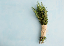 A Bunch Of Fresh Green Twigs Of Rosemary Wrapped In Paper And Tied With A Rope Lies On A Blue Background. Seasonings. Copy Space
