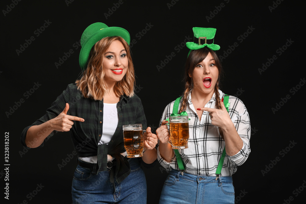 Funny young women with beer on dark background. St. Patrick's Day celebration