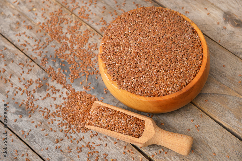 Bowl with flax seeds and scoop on wooden background