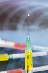 Syringe with a drop of medicine on the background of lung x-ray photo. Pneumonia medication concept, coronavirus vaccine, curing diseases, protecting. Closeup, selective focus