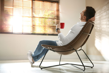 Canvas Print - Young man with cup of drink relaxing near window at home. Space for text