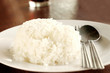 Defocused and blur image of white rice thai in plate with spoon and fork on wooden table.